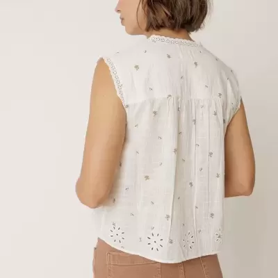 Blusa branca sem mangas bordada com flores douradas e recortes em formato de flores na parte inferior.
