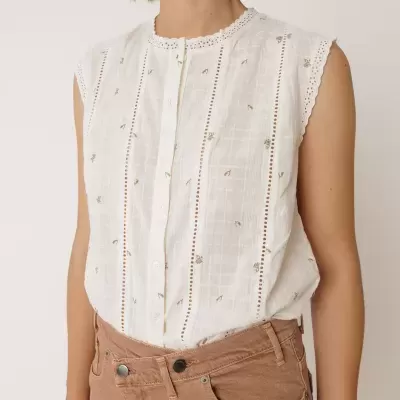 Top branco bordado com botões e calças de ganga castanhas.