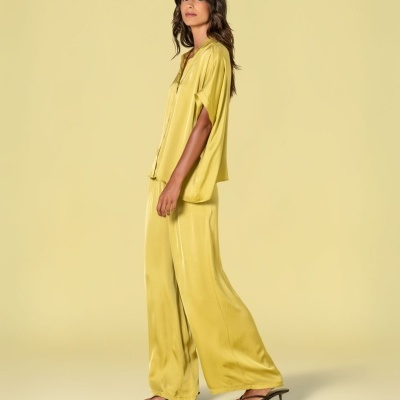 Mulher a usar conjunto amarelo acetinado com sandálias pretas sobre fundo amarelo