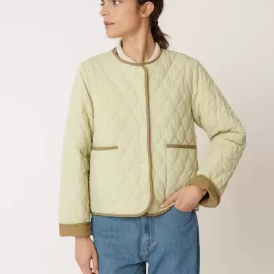 Casaco acolchoado bege com bordas castanhas em mulher com jeans azuis