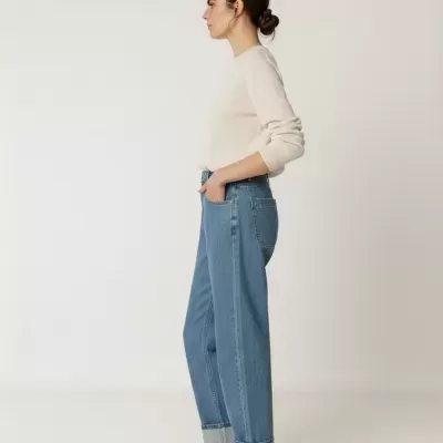 Mulher de perfil com camisola bege, jeans azuis e sapatilhas cinzentas