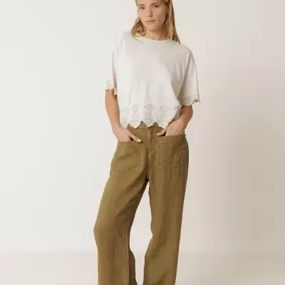 Mulher com t-shirt branca bordada e calças castanhas largas em fundo branco