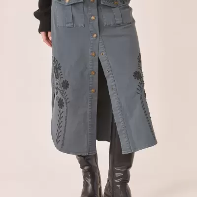 Saia azul-acinzentada com botões dourados e bordados florais, botas pretas cano alto.