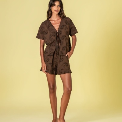 Mulher com conjunto castanho de camisa e calção com padrão bordado e sandálias pretas de salto fino