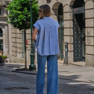 Camisa azul às riscas e calças de ganga largas vista de costas em cidade.