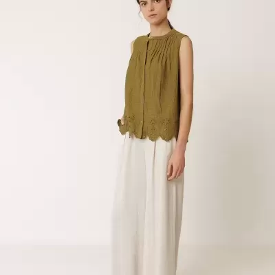 Mulher com blusa verde oliva sem mangas e calças largas brancas.