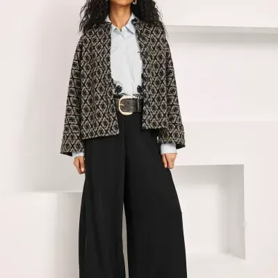 Mulher com conjunto de casaco padrão, camisa bordada e calças largas pretas