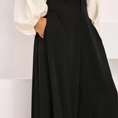 Calças largas pretas com cós alto vestidas com camisa branca de mangas bufantes.