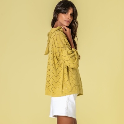 Camisola amarela de malha com padrão de pontos usada com calções brancos em fundo amarelo