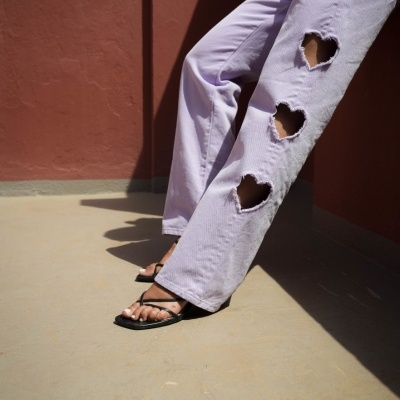 Calças lilás com rasgões em forma de coração e sandálias pretas em ambiente exterior terra