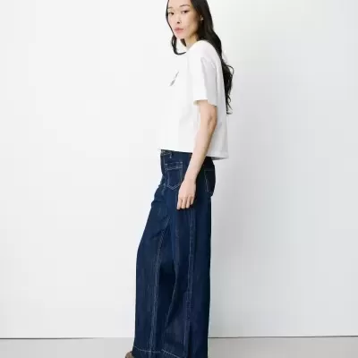 Mulher com camiseta branca e calças largas de ganga azul