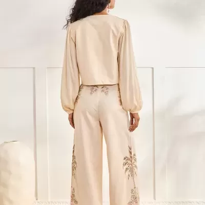 Calças creme largas com bordado floral e camisa creme de mangas compridas vistas de costas