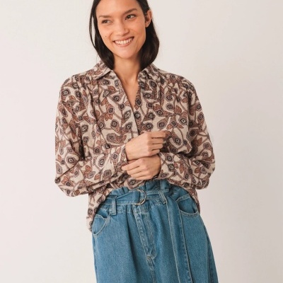 Mulher com blusa de padrão de folhas castanho-bege e calças de ganga com cinto azul