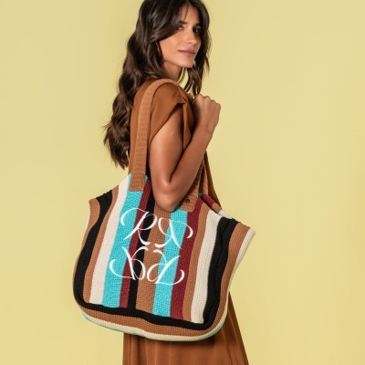 Mulher com vestido castanho a usar sacola de tecido tricotado com riscas coloridas e letras PZ