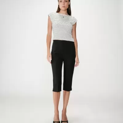 Mulher a usar camisola branca de riscas pretas e calças capri pretas.