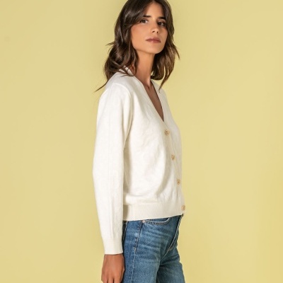 Mulher vestindo cardigan branco e jeans azul com fundo amarelo