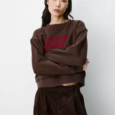Mulher vestindo sweatshirt castanha com texto vermelho e calças de veludo castanhas
