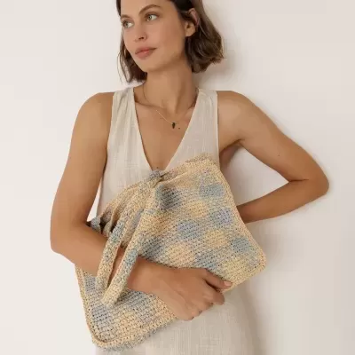 Mulher com vestido bege a segurar mala trançada bege e azul