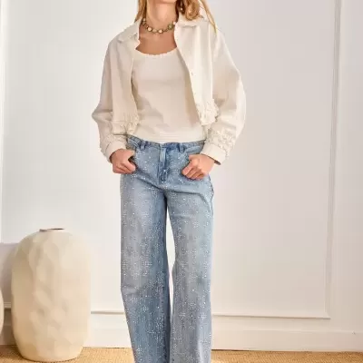 Calças de ganga azul claro com padrão floral branco e pérolas e roupa branca em interior com vaso creme