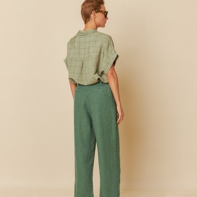 Pessoa de costas com camisa verde clara xadrez e calças verdes escuras, usando sandálias e óculos escuros