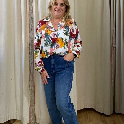 Pessoa a usar camisa floral, calças de ganga e ténis num ambiente com cortinas bege