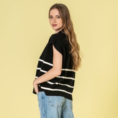 Mulher com camisola preta às riscas brancas e calças de ganga azuis claras contra fundo amarelo