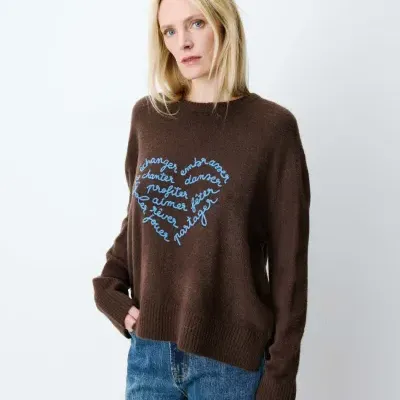 Mulher com sweatshirt castanha com bordado azul em forma de coração e calças de ganga azuis
