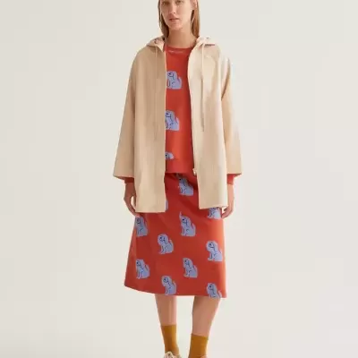 Mulher com casaco bege, roupa vermelha com padrão azul e sapatilhas castanhas