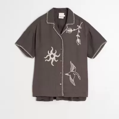 Camisa castanha escura com bordados brancos e botões frontais.