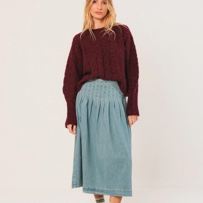 Mulher com camisola de malha vinho, saia azul clara, meias castanhas e verdes e sapatilhas brancas