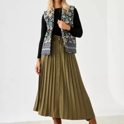 Mulher vestindo gorro bege, colete estampado, camisola preta, saia plissada verde oliva e botas castanhas