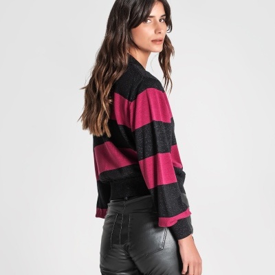 Mulher de lado com camisola de riscas preta e rosa e calças pretas brilhantes