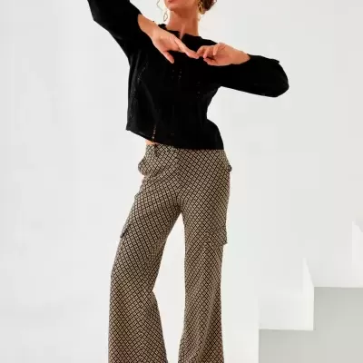Mulher com blusa preta de renda e calças largas padrão geométrico bege e preto.