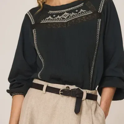 Blusa preta com bordados e renda branca, saia bege e cinto castanho