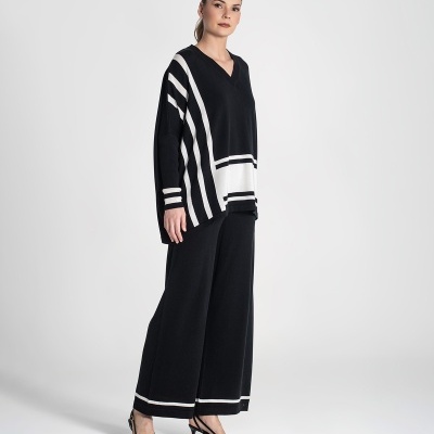 Mulher com conjunto de tricô preto e branco, sapatos pretos de salto, em fundo cinzento claro