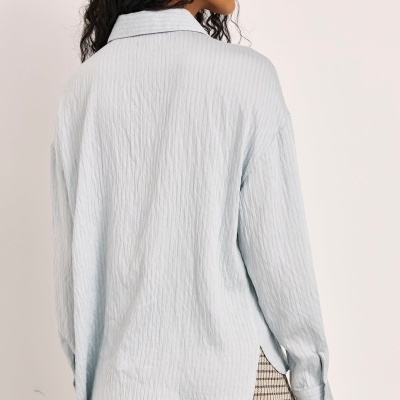 Blusa azul-claro texturizada de manga comprida vista de costas com saia rodada aos quadrados preto e bege