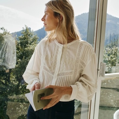 Camisa feminina branca com detalhes rendados em ambiente iluminado junto a janela