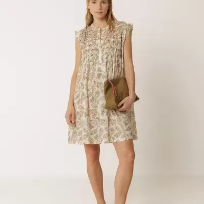 Mulher com vestido curto branco e padrão paisley segurando bolsa castanha