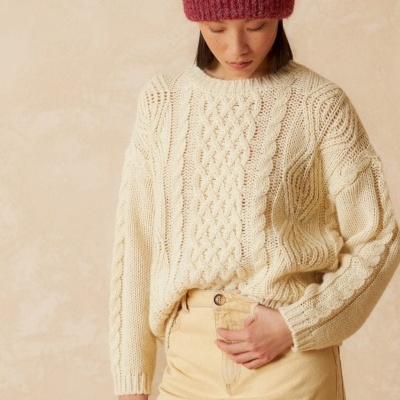 Mulher com camisola bege de malha, saia bege e gorro vermelho.