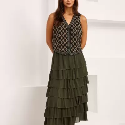 Mulher com colete preto floral, saia verde e botas pretas