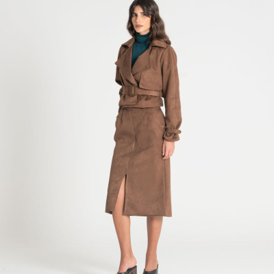 Mulher vestindo conjunto castanho com casaco e saia midi com fenda, camisa verde e sapatos pretos de salto alto.