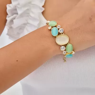 Pulseira dourada com pedras coloridas num pulso sobre regata branca com folhos