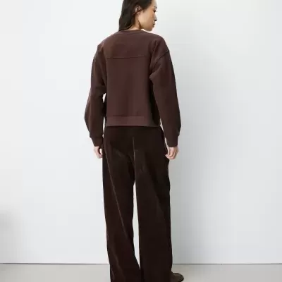 Mulher vista de costas com sweatshirt e calças castanhas em fundo branco