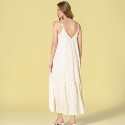 Vestido comprido creme com alças finas e pregas, visto de costas, com sandálias cor creme em fundo amarelo