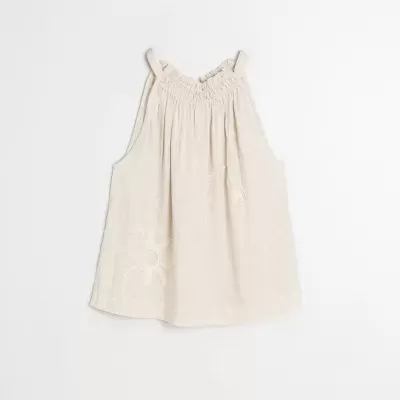 Blusa de alças finas bege com bordados florais e franzido no decote sobre fundo branco.