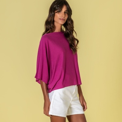 Mulher com blusa rosa forte e calções brancos sobre fundo amarelo claro