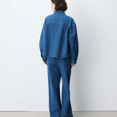 Conjunto azul com padrão geométrico, camisa de gola alta e calças largas de costas.