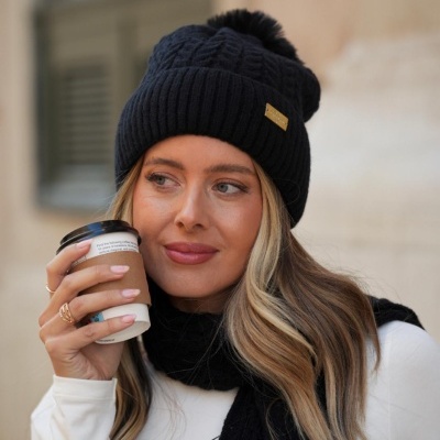 Mulher com gorro e cachecol pretos e camisola branca segurando copo de café