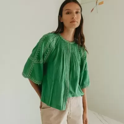 Blusa verde bordada com calções beiges num ambiente minimalista.