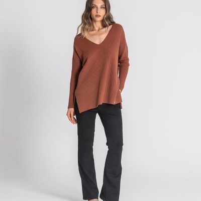 Mulher com camisola castanha e calças pretas em fundo branco
